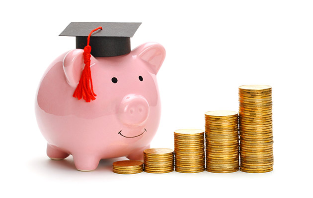 Piggy bank in graduate cap near stack of coins.